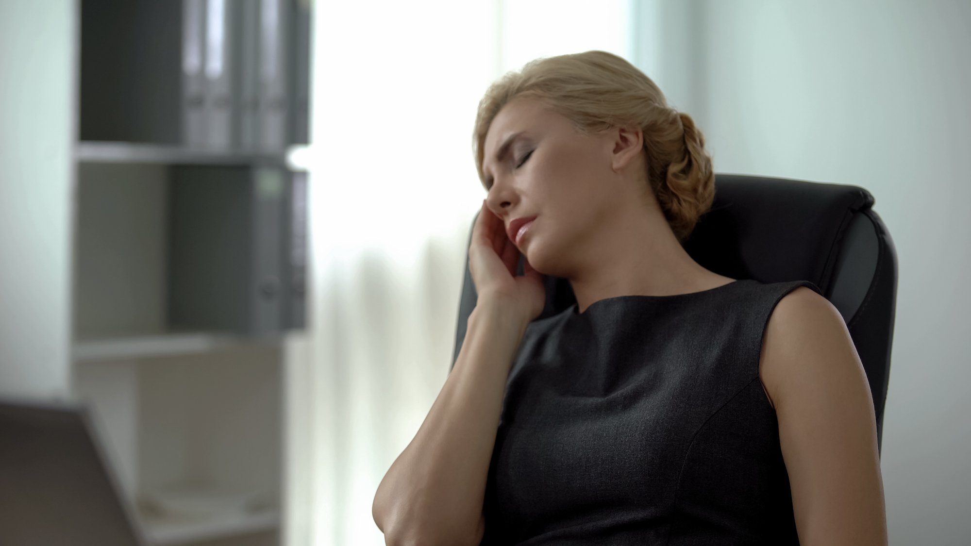 woman sitting in office chair holding face because of dental pain