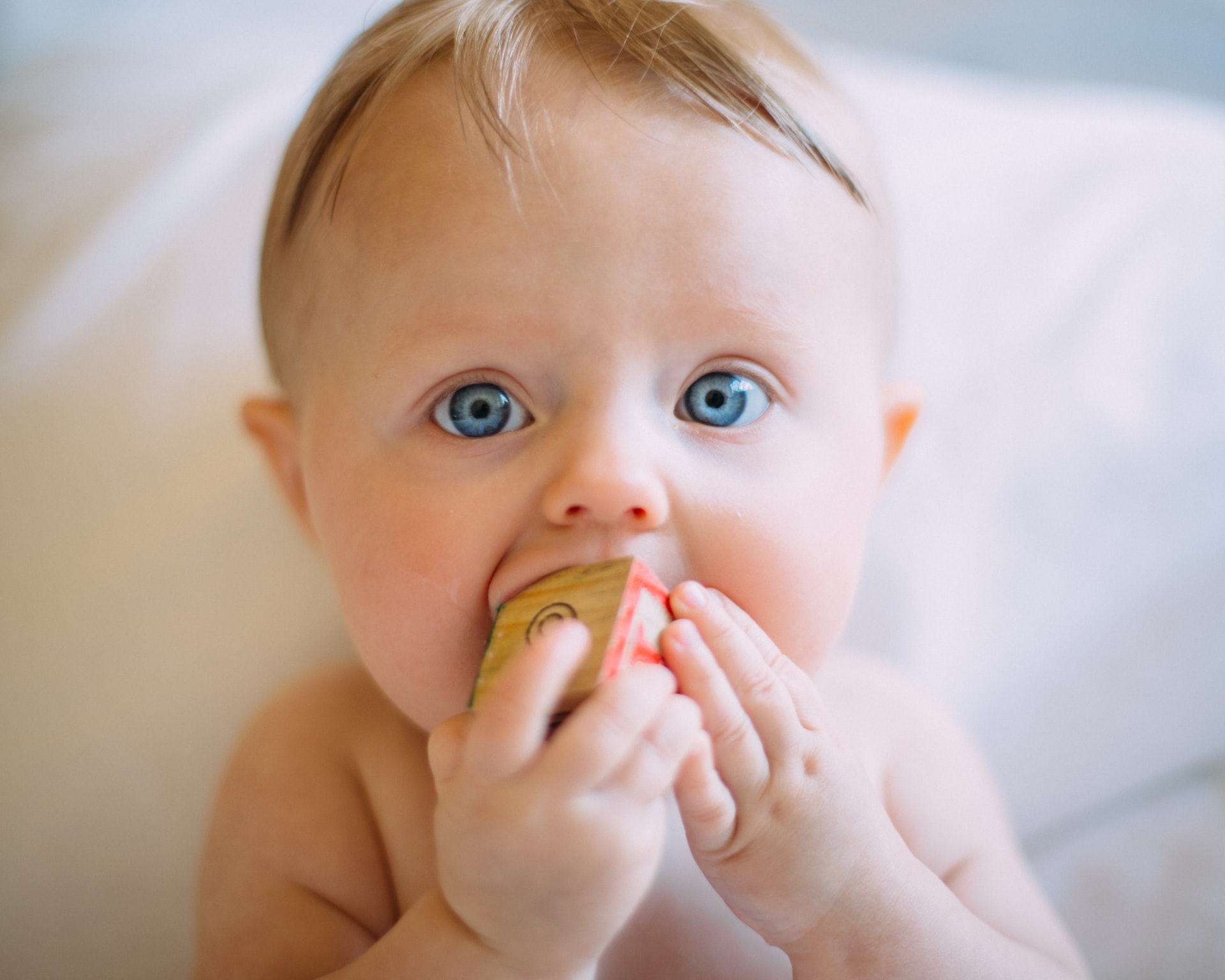 close up of teething baby with blonde hair and blue eyes