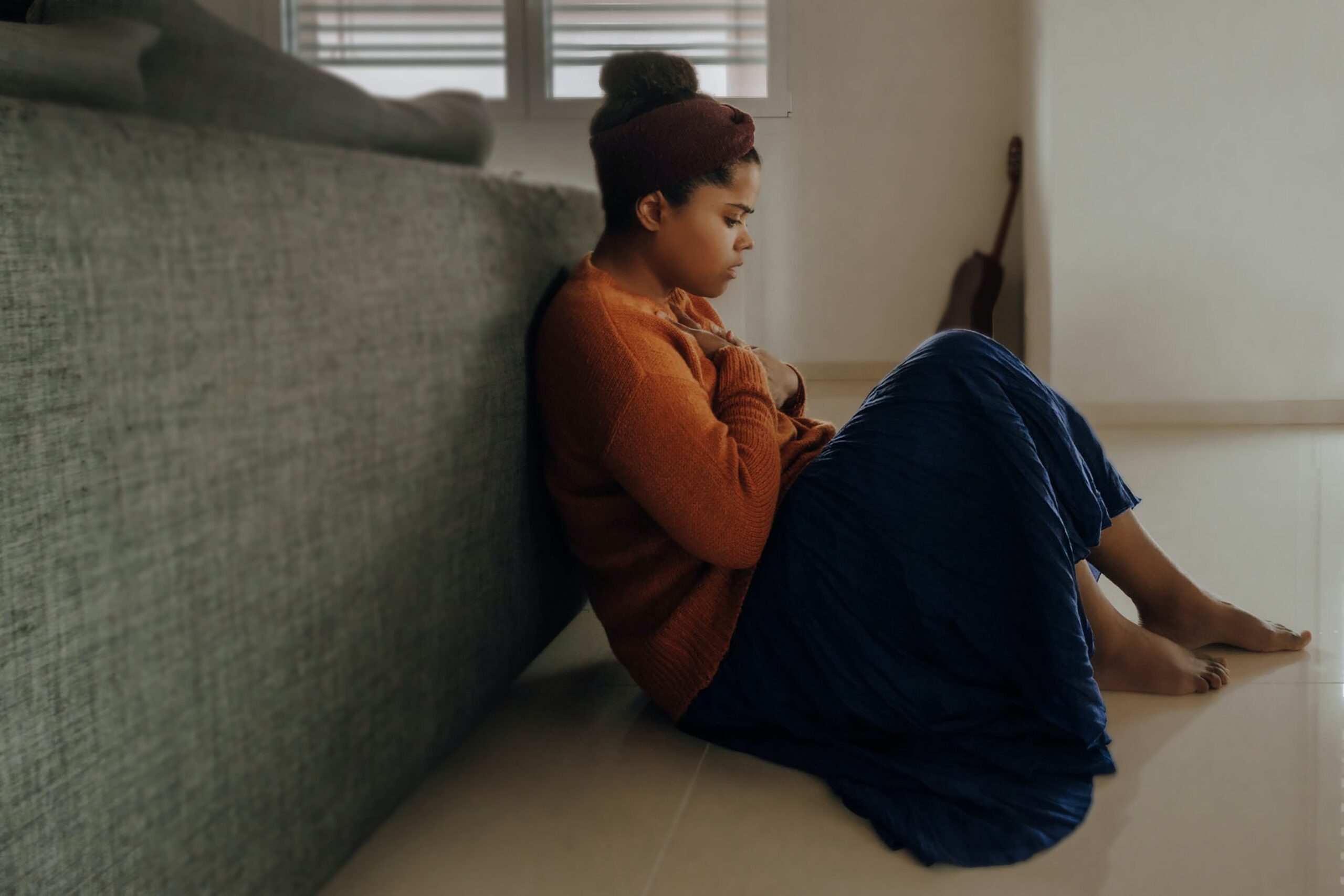 A young woman sits on the floor and clutches her chest, indicating dentophobia before a dental appointment