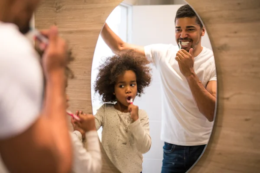 father and daughter brushing teeth in mirror