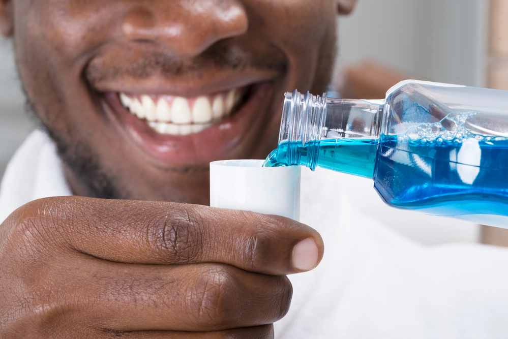 black man pouring blue mouthwash into cup