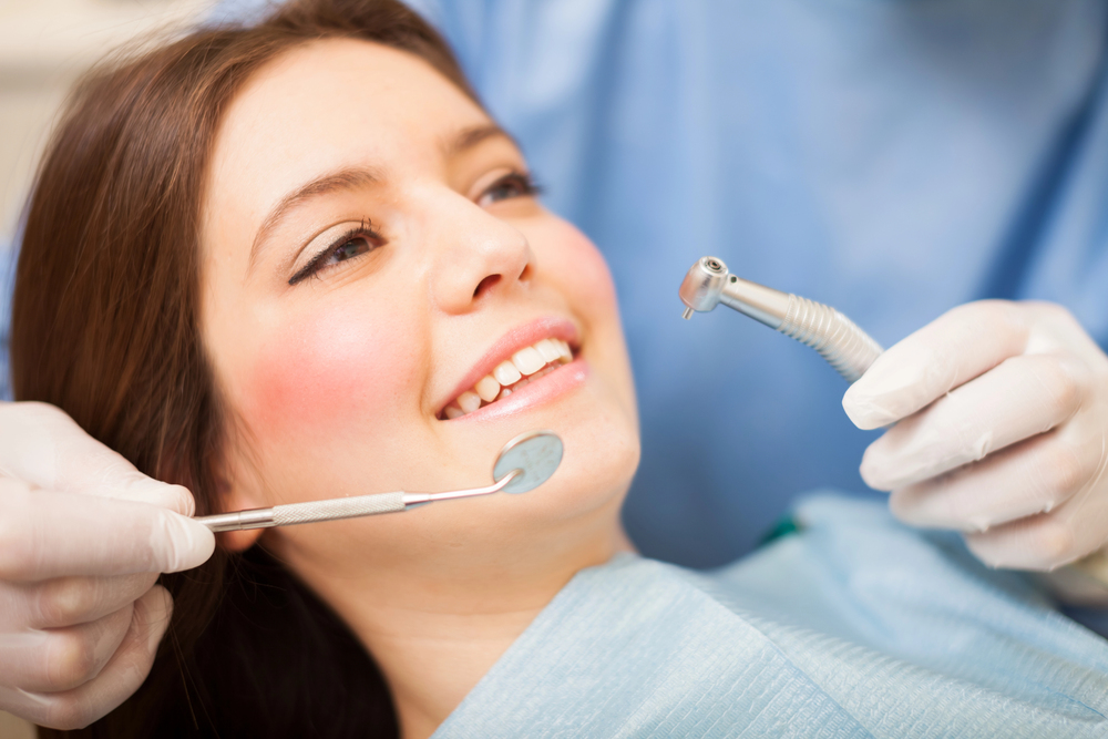 young woman in a dental chair, dentist holding dental mirror and toothbrush over woman's teeth